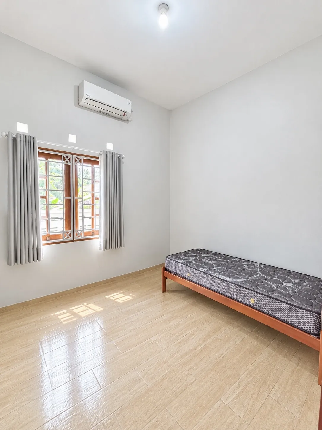 Bright single room with an air conditioner, a window with curtains and a single bed