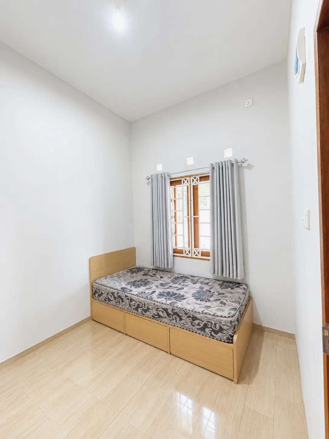 Single room with a bed that has storage drawers underneath and a window with curtains